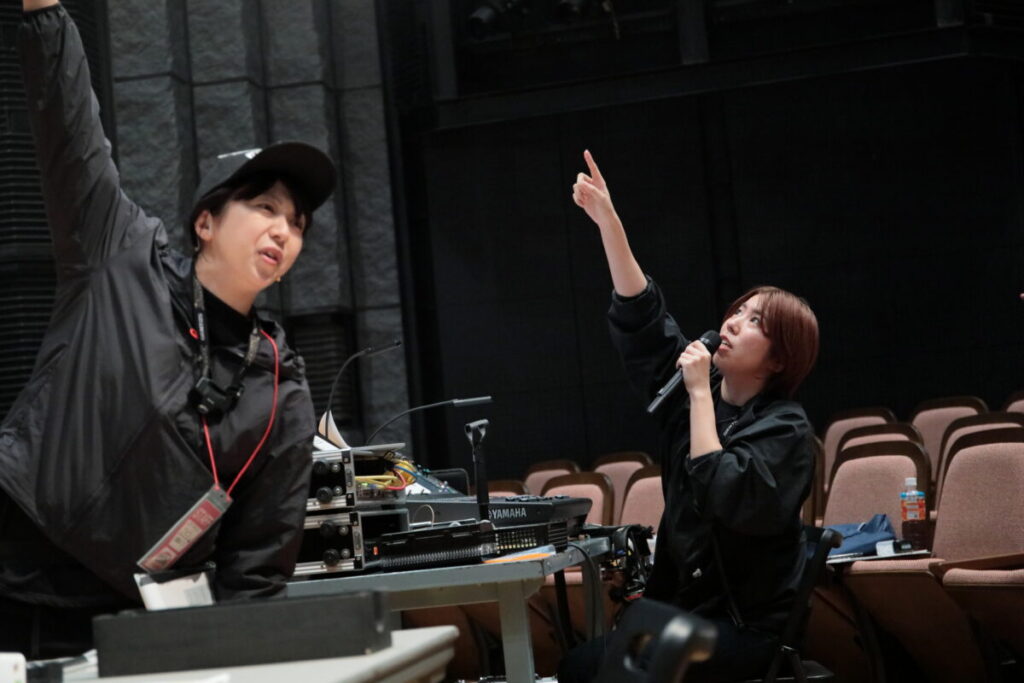 黒い服装(スタッフ服)の女性二人が天井を指差して話している